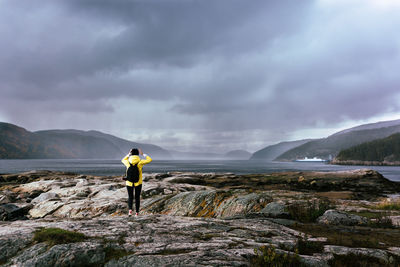 Rear view of woman standing on rock against sea and sky