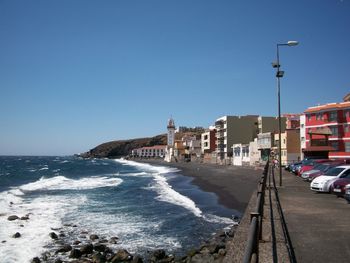 Buildings by sea against clear blue sky