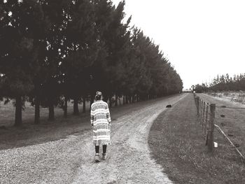 Rear view of woman walking on road by trees against clear sky