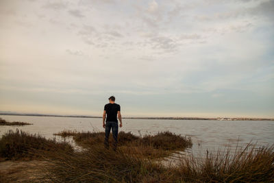 Rear view of man standing at lakeshore against sky