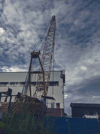 Low angle view of crane by building against sky