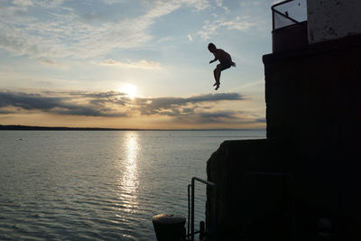 Silhouette man jumping in sea against sky during sunset