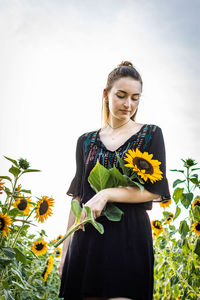Young woman standing by sunflower against sky