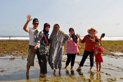 Full length of friends standing on beach against sky