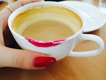 Cropped hand of women holding lipstick stained coffee cup on table