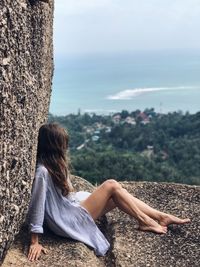 Side view of woman sitting on cliff against sea at ko samui