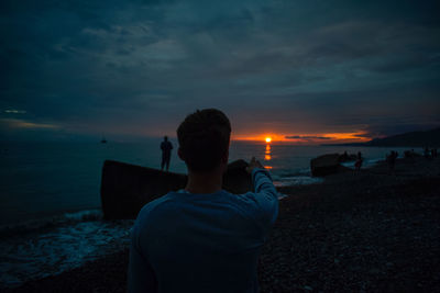 Rear view of man standing by sea against sky during sunset