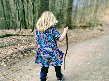 Rear view of girl holding stick and walking on footpath