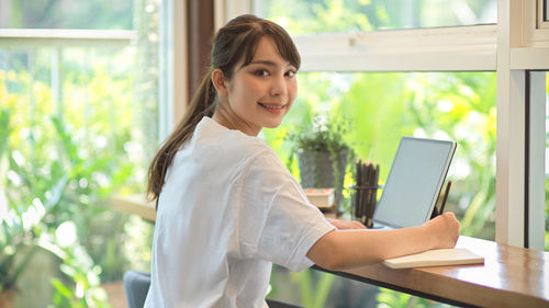 Portrait of smiling woman standing by window