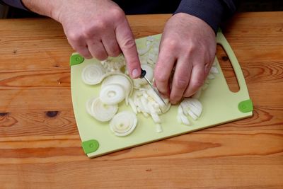 Cropped hands of man cutting onions on board