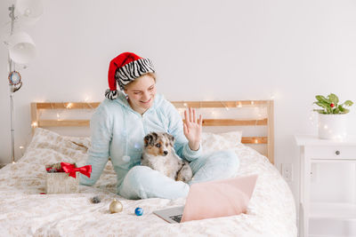 Young woman and dog sitting on bed at home