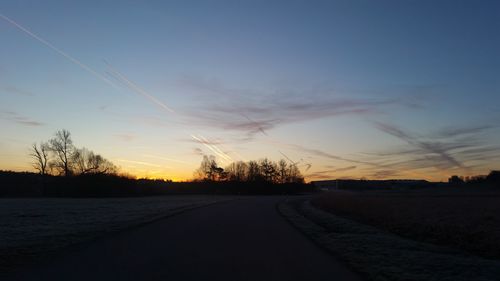 Road amidst field against sky during sunset