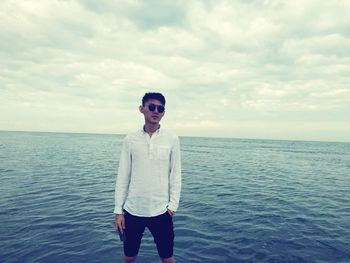 Young man standing in sea against sky