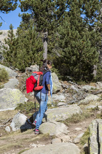 Side view of woman with backpack hiking on rocks against trees