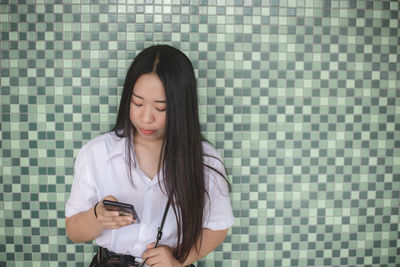 Young woman using mobile phone against wall