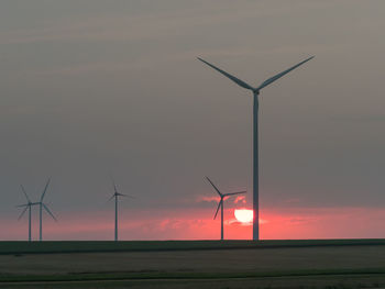 Windmills on field against sky during sunset