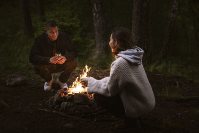 Couple sitting by campfire in forest