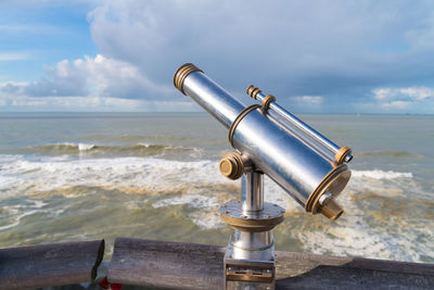 Coin-operated binoculars by sea against sky