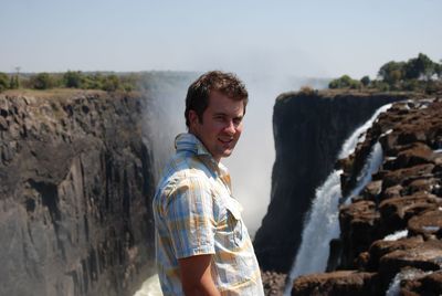 Portrait of smiling man standing against waterfall