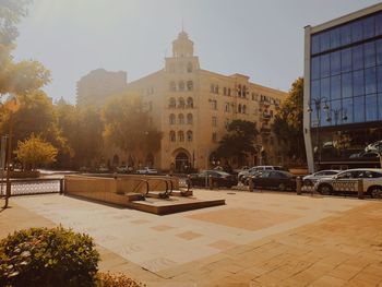 Cars on road by buildings in city against sky