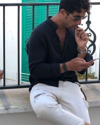 Man smoking while using mobile phone against railing