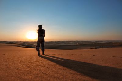 Silhouette woman walking on beach against clear sky during sunset