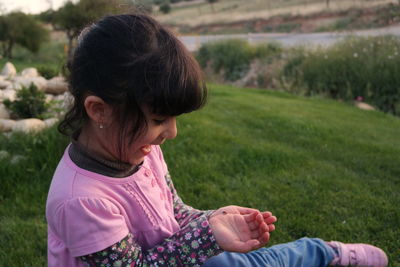 Curious girl looking at insect while sitting on grassy hill