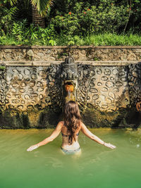 Rear view of woman wearing bikini standing against fountain