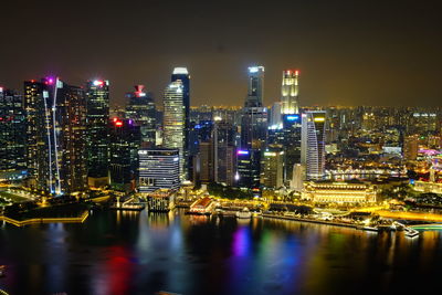 Illuminated cityscape by river against sky at night