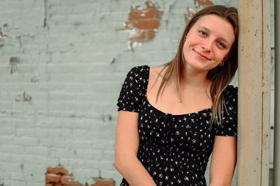 Portrait of young woman standing against wall