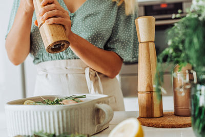 Woman with a pepper grinder seasoning food in a tray