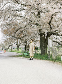 Full length of young woman standing on road by cherry tree