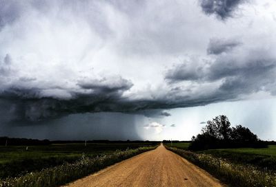 Road passing through field against cloudy sky