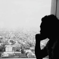 Man sitting on seat in city against sky