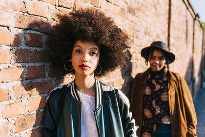 Female friends standing by brick wall during sunny day