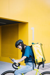 Smiling delivery woman with backpack using smart phone on bicycle
