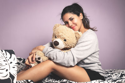 Portrait of young woman holding toy while sitting against wall