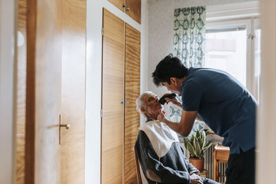 Side view of male care assistant trimming mustache of senior man at home