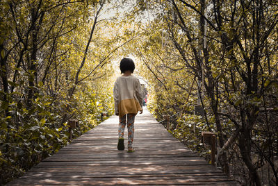 Rear view of girl walking on footpath in forest