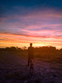Rear view of silhouette man standing on field against sky during sunset