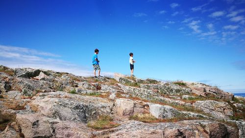 Low angle view of siblings walking on rocky hill against sky