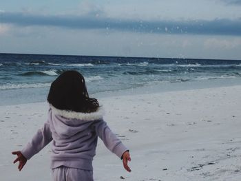 Rear view of girl playing with sand at beach against sky