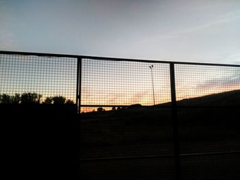 Silhouette fence against sky during sunset