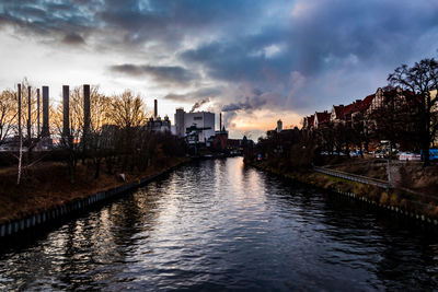 River amidst buildings in city against sky at sunset