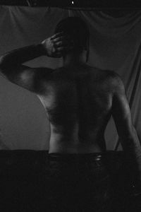 Rear view of shirtless man standing against wall