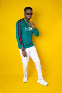 Young man wearing sunglasses standing against yellow background