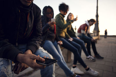 Friends using phone while sitting on railing at city square