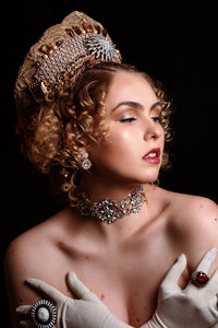 Portrait of a young woman wearing crown standing against a black background