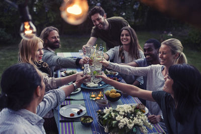 Happy multi-ethnic friends toasting drinks at dinner table in yard