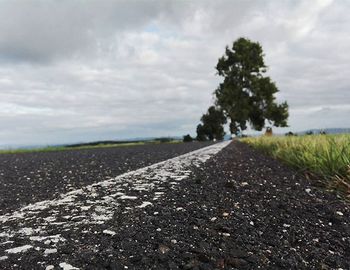 Road passing through field against cloudy sky